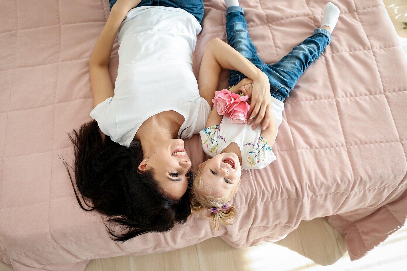 A joyful moment of a mother and daughter lying on a pink bed, smiling and connecting.